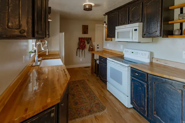 Kitchen featuring wood-finish flooring, wood countertops, built-in cabinetry, a single basin sink, and white appliances
