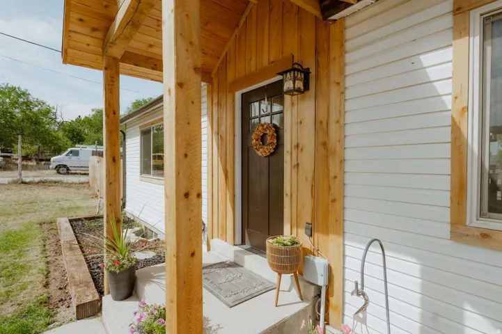 Covered front porch with natural wood posts, wood-finish siding accents, white horizontal siding, and a dark entry door with windowpanes