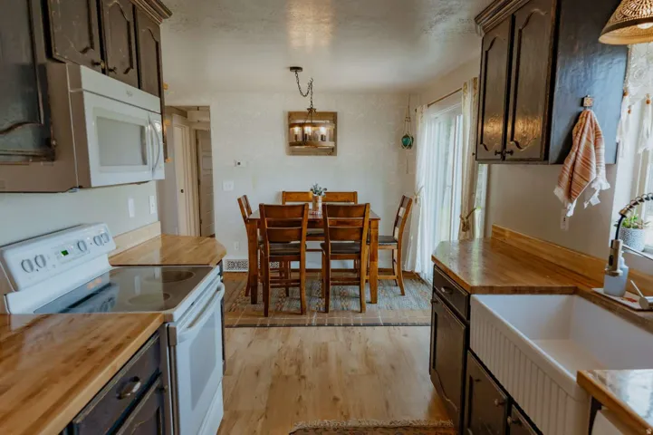 Wood-finish countertops, dark cabinetry, white built-in microwave, and a white farmhouse sink