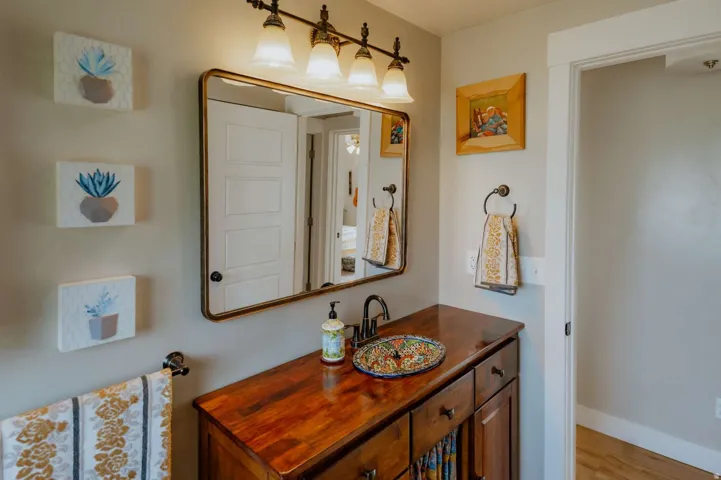 Wood-finish vanity with a vessel sink, wall-mounted faucet, and overhead vanity lighting