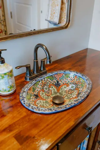Wood-finish countertop with an intricately patterned vessel sink, bronze-finish faucet, and coordinating bronze-finish drain