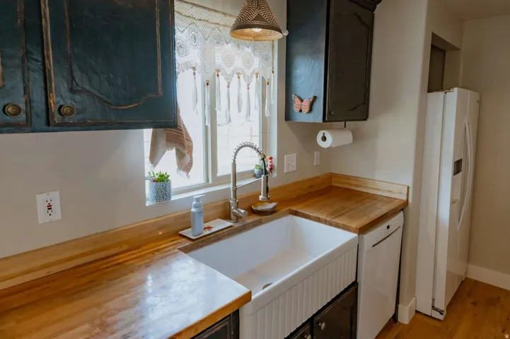 Farmhouse sink with a gooseneck faucet, wood-finish countertops, and upper dark cabinetry