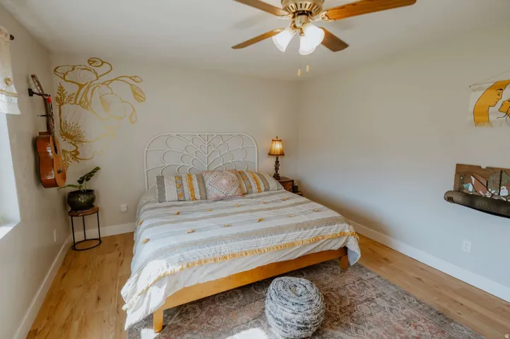 Wood-finish flooring with white baseboards, a ceiling fan with integrated lighting, and a wall-mounted shelf