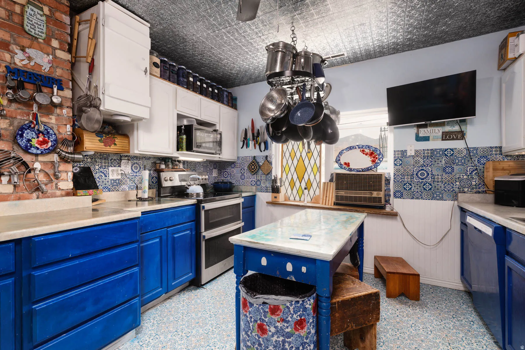 Kitchen featuring blue base cabinetry, white upper cabinetry, mosaic tile backsplash, and a tin-finish ceiling