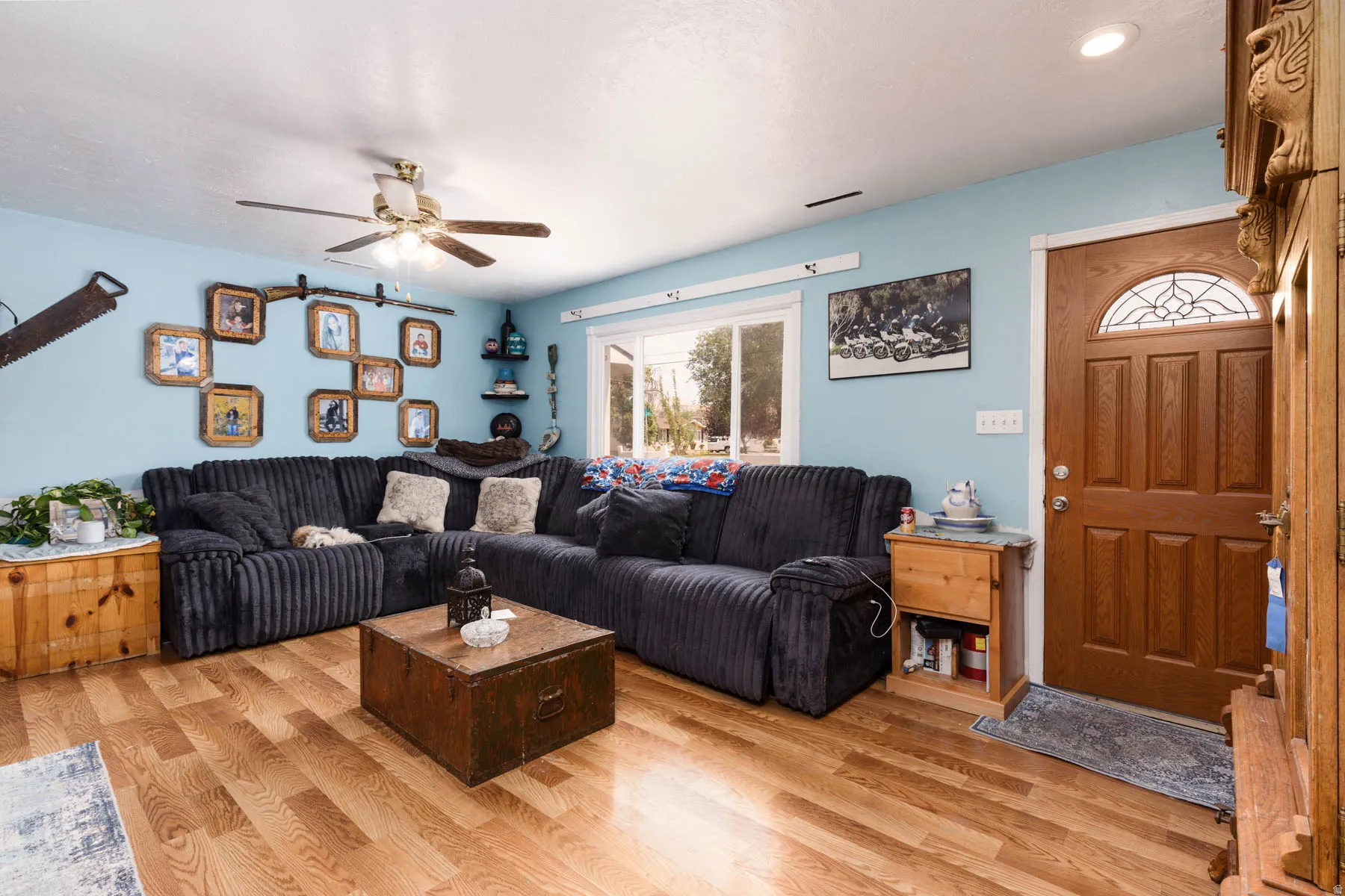 Light-filled living room featuring a sectional layout with ribbed upholstery, hardwood flooring throughout, and soft-close ceiling fan