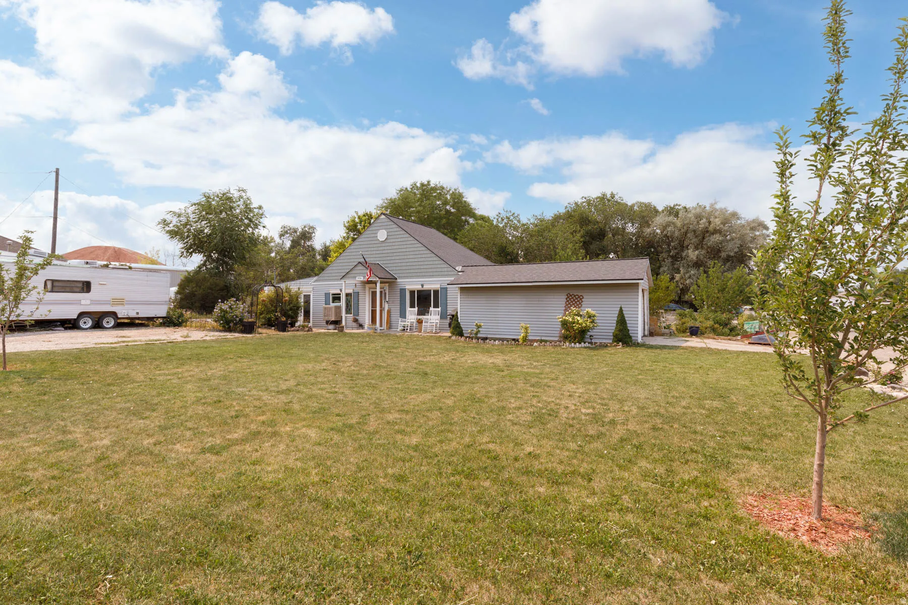 Gable roof home with light siding, front porch, attached single-story structure, and expansive front lawn