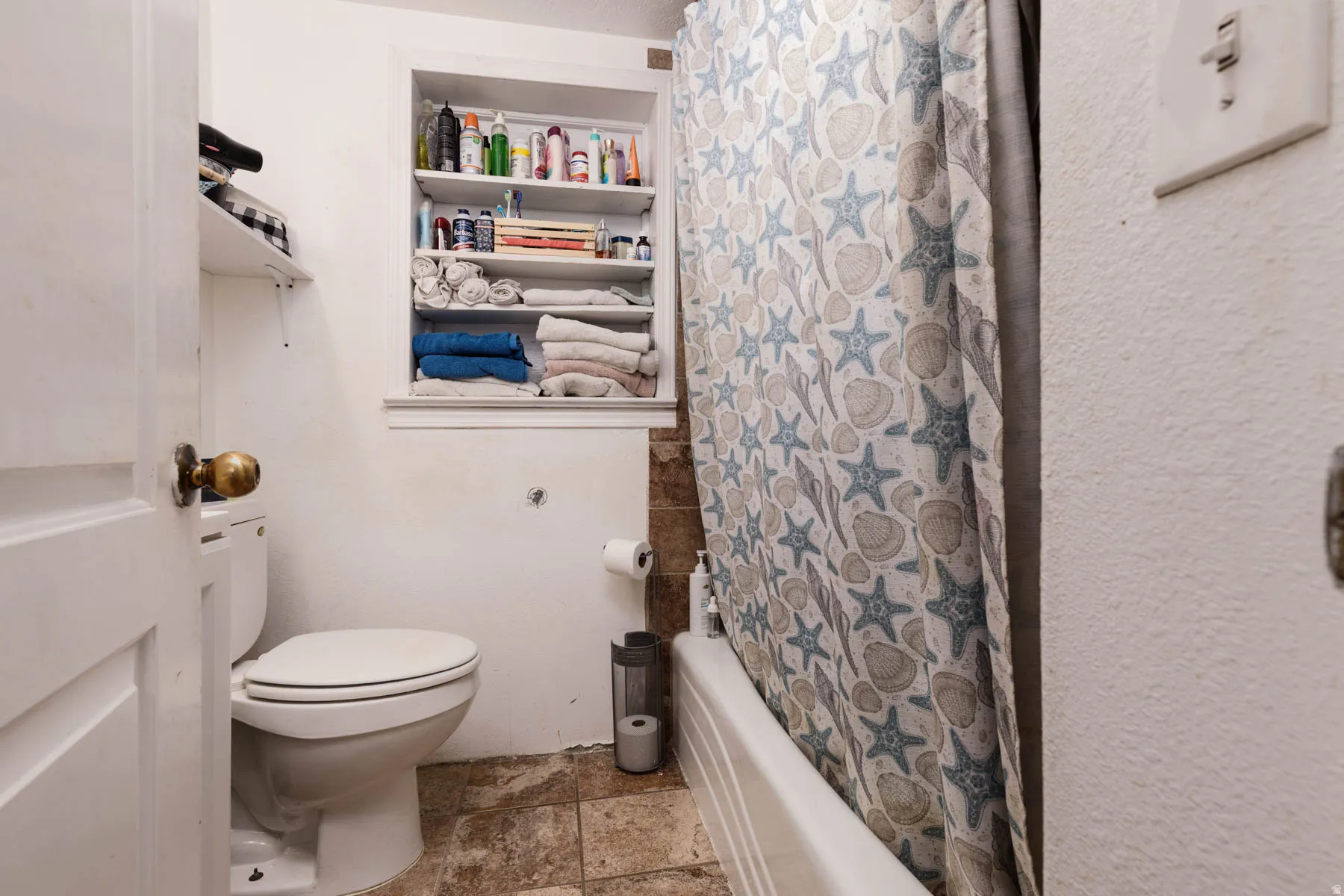 Compact bathroom featuring a ceramic toilet, tile flooring, and built-in shelving with storage