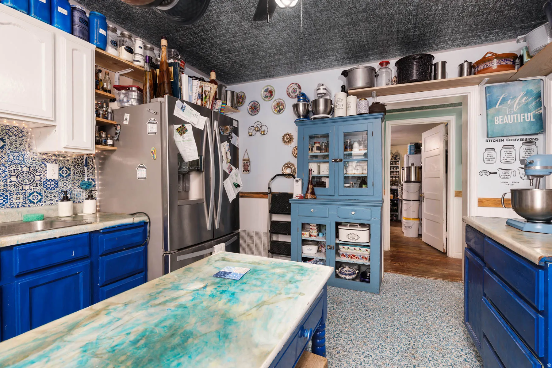 Kitchen featuring white upper cabinetry, blue lower cabinetry, stainless steel refrigerator, patterned backsplash, and patterned flooring