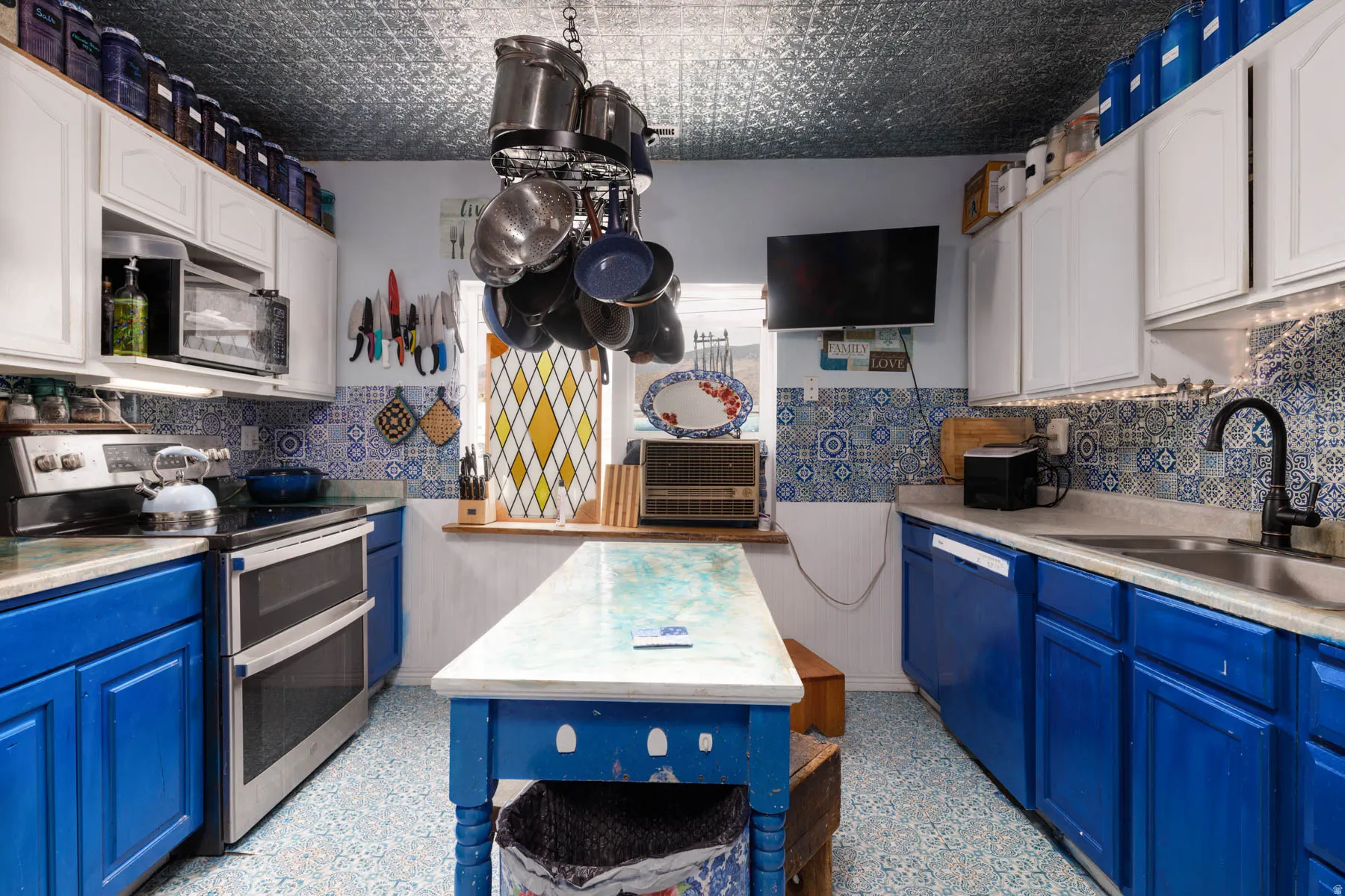 Kitchen featuring stainless steel appliances, patterned backsplash tiling, a central island, and white upper cabinetry contrasted with blue lower cabinetry