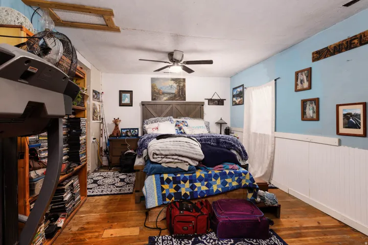 Hardwood flooring, painted blue walls with white wainscoting, wood-paneled bed frame, and ceiling fan with integrated lighting