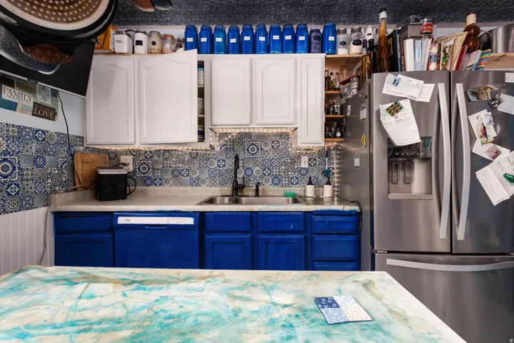 Patterned tile backsplash, stainless steel refrigerator, white upper cabinetry, blue lower cabinetry, built-in dishwasher