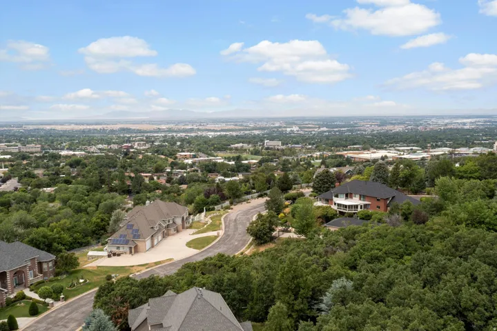Expansive aerial perspective showcasing the residence nestled within mature landscaping, complemented by manicured grounds, curved driveway with light-colored pavement, and a sprawling suburban setting with extensive tree coverage throughout the surroundi