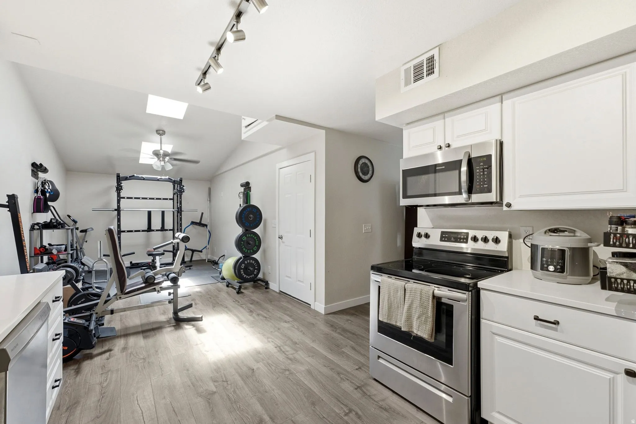 Vaulted ceiling with skylights, wood-finish flooring, white cabinetry, stainless steel range, and stainless steel microwave