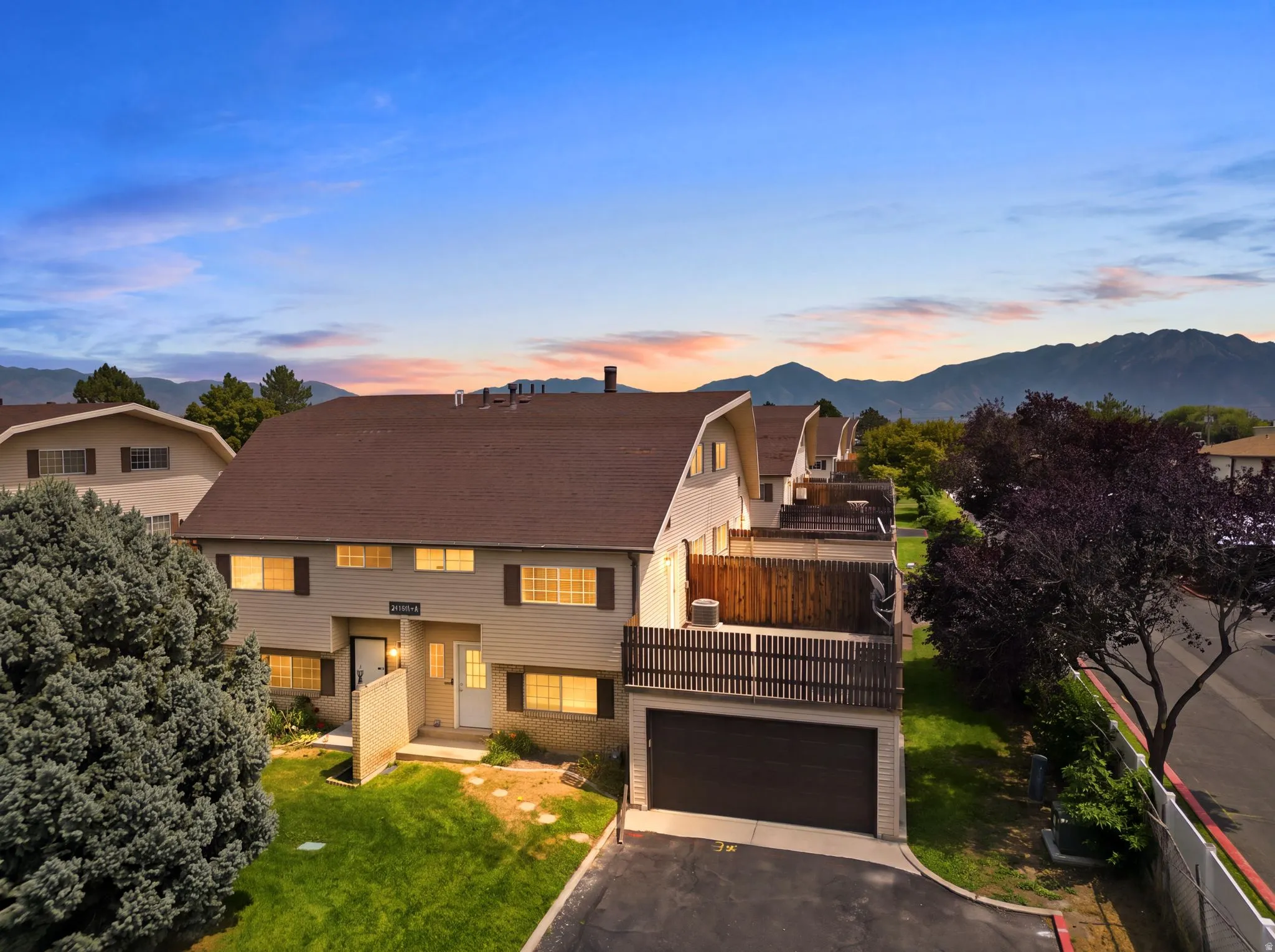 Modern two-story residence featuring a dark-shingled pitched roof, multi-pane illuminated windows, and a two-car garage with dark paneling