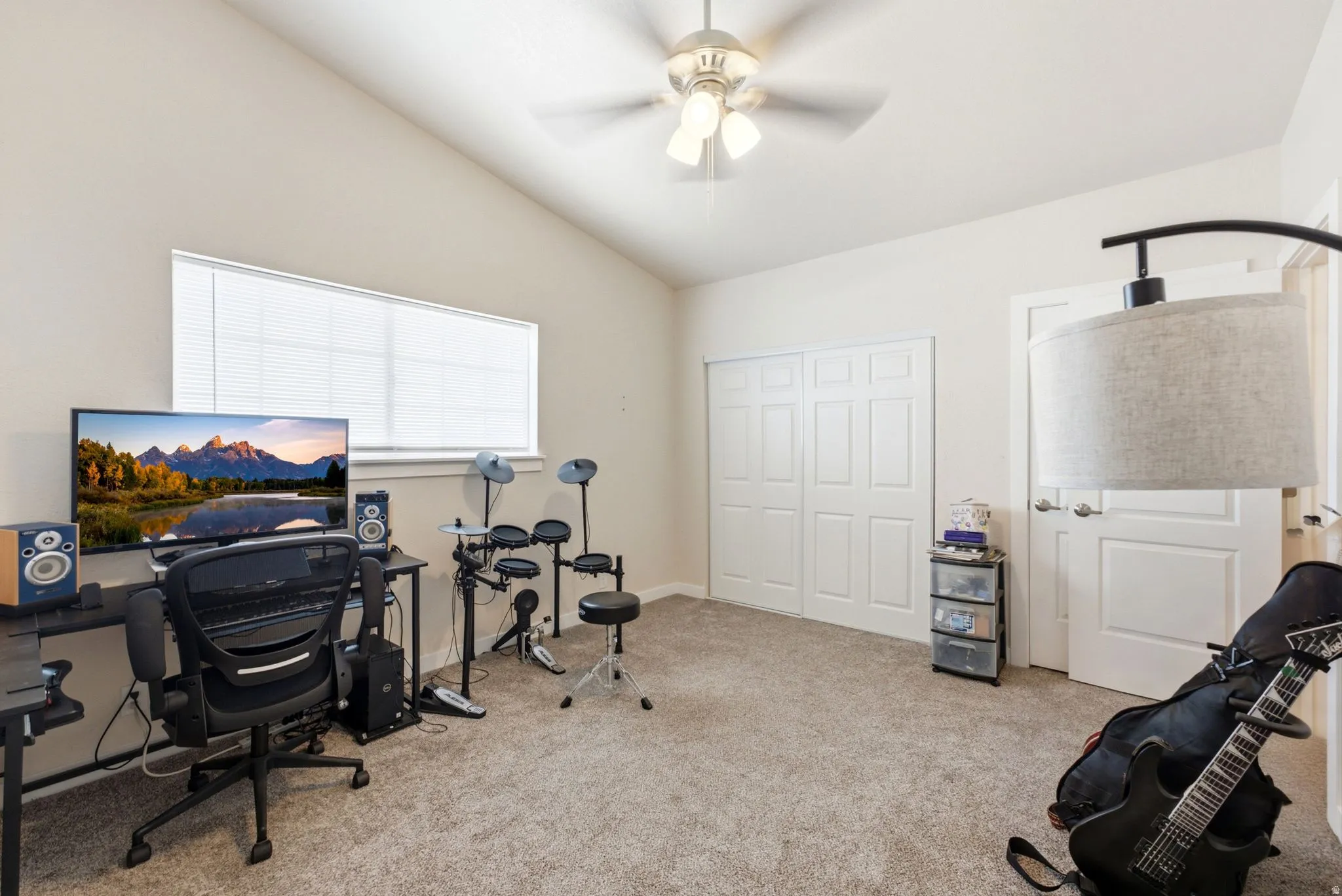 Spacious bonus room featuring neutral carpet flooring, multiple white six-panel closet doors, ceiling fan with integrated lighting, and large windows allowing natural light throughout the space