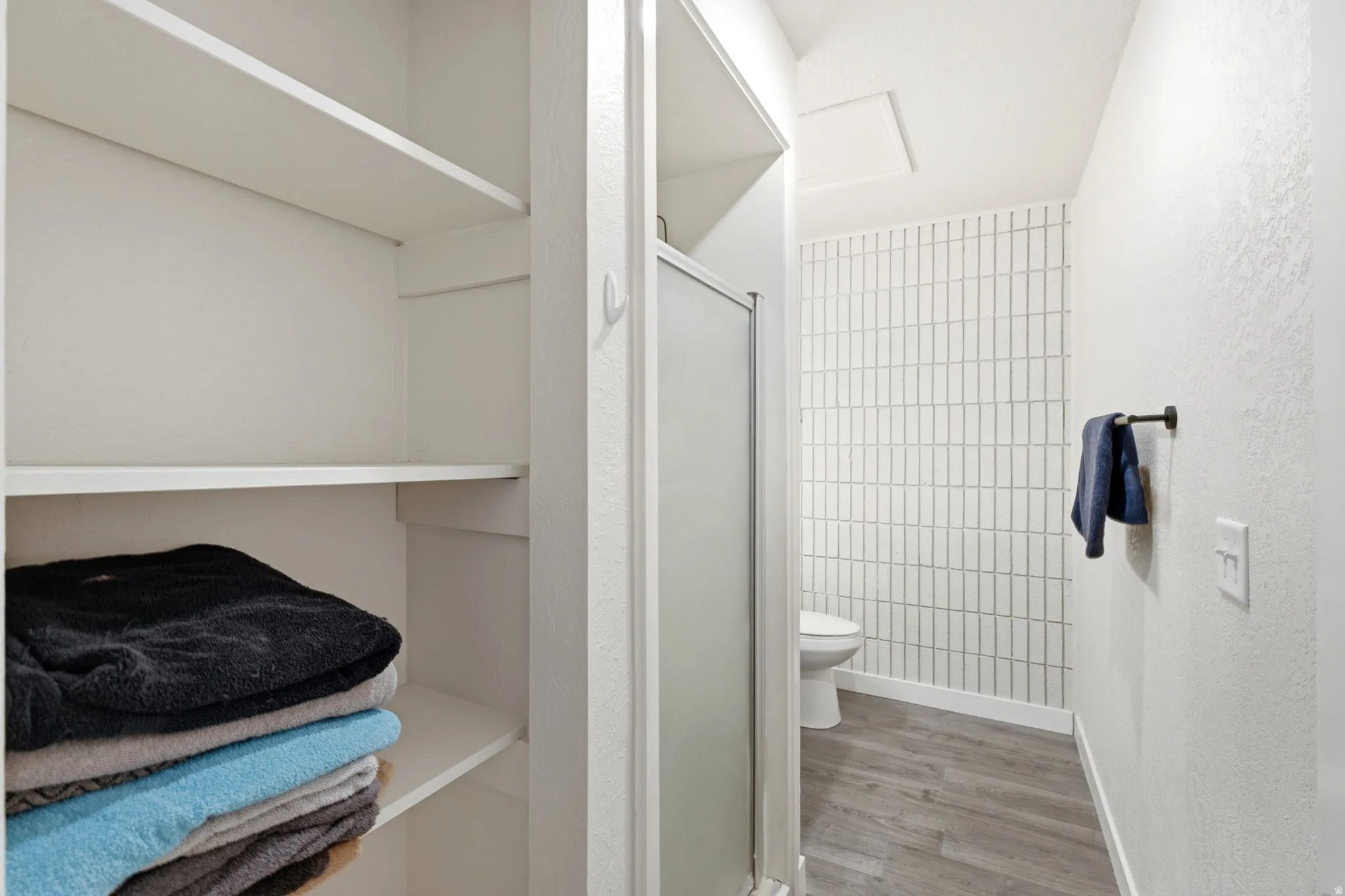 Efficient bathroom layout featuring white subway tile walls, wood-finish flooring, and a toilet with chrome fixtures