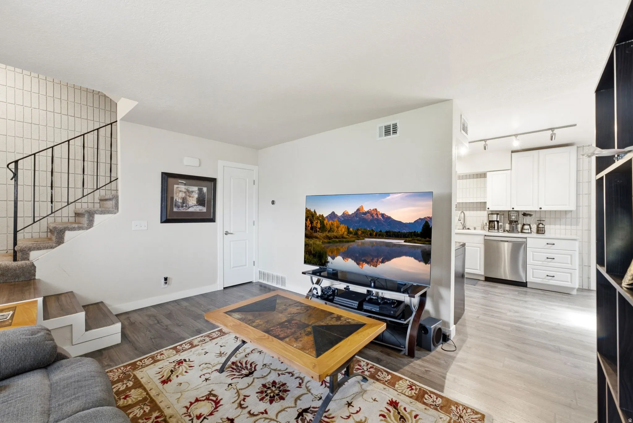 Open-concept living space featuring hardwood flooring, a gas fireplace with built-in entertainment cabinetry, and a well-appointed kitchen with white cabinetry and stainless steel appliances