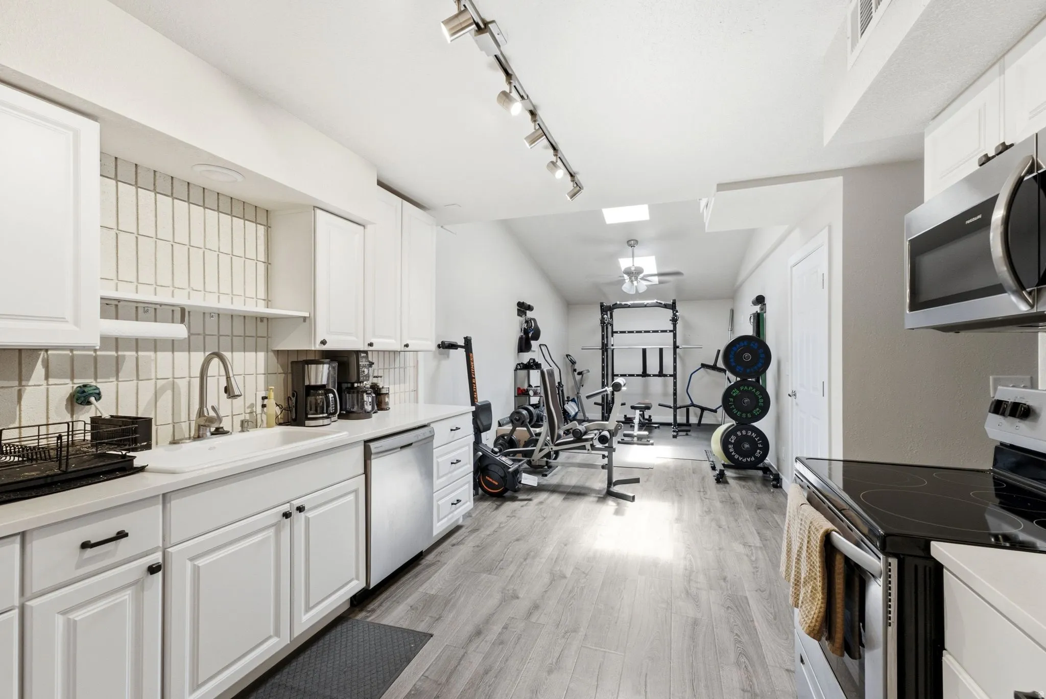 White cabinetry with dark hardware, a subway tile backsplash, stainless steel appliances, and wood-finish flooring