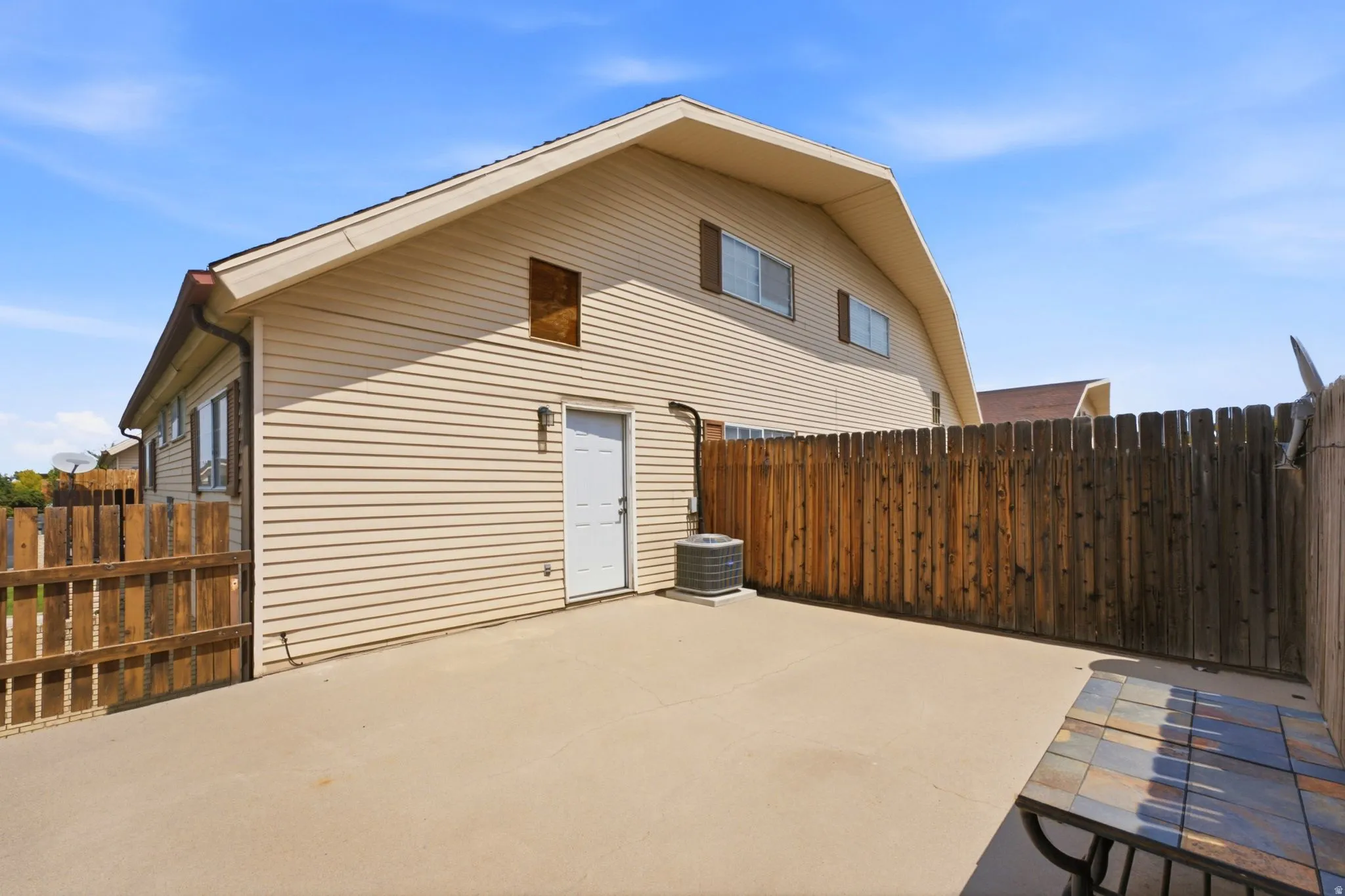 Siding exterior featuring a gambrel roofline, a ground-level access door, and a privacy fence