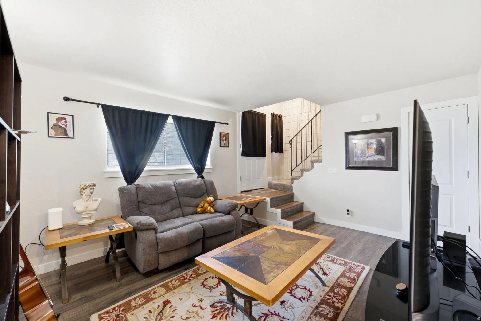 Wood-finish flooring throughout, white walls, and a staircase with an iron railing