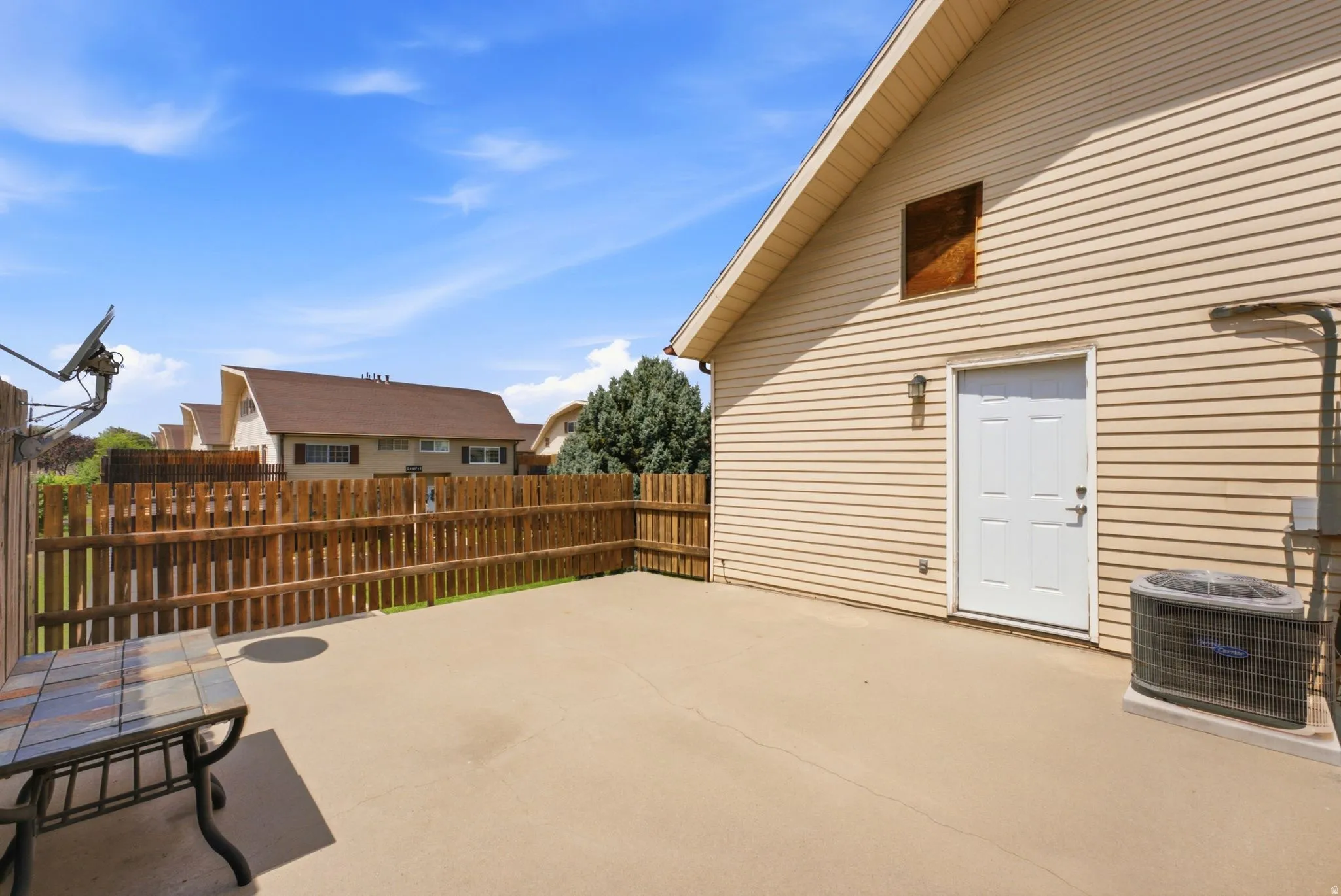 Expansive concrete patio with wooden privacy fencing, mature landscaping, and direct access to the home's exterior