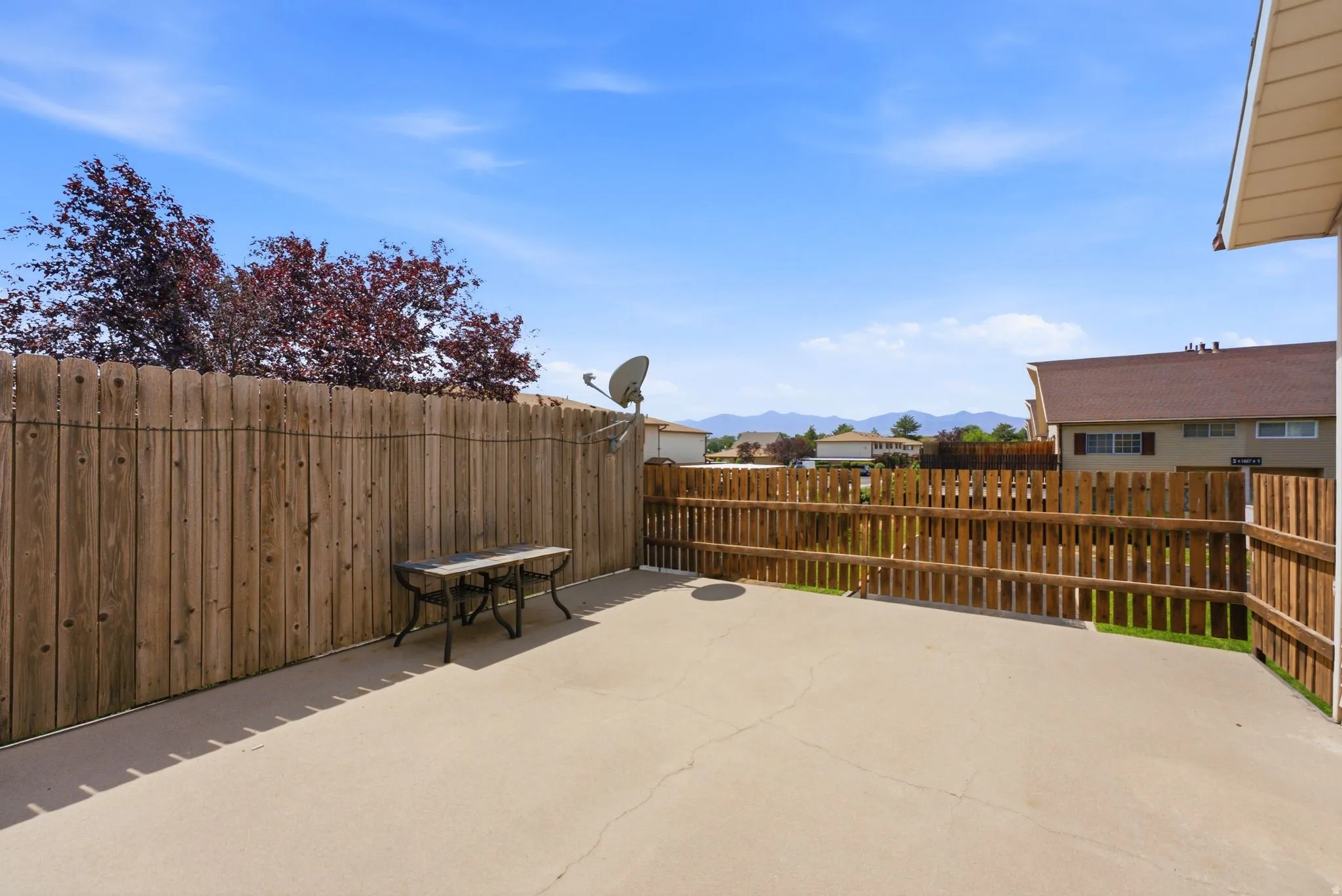 Expansive composite deck featuring wood-finish railing and fencing, anchored by mature landscaping and mountain backdrop