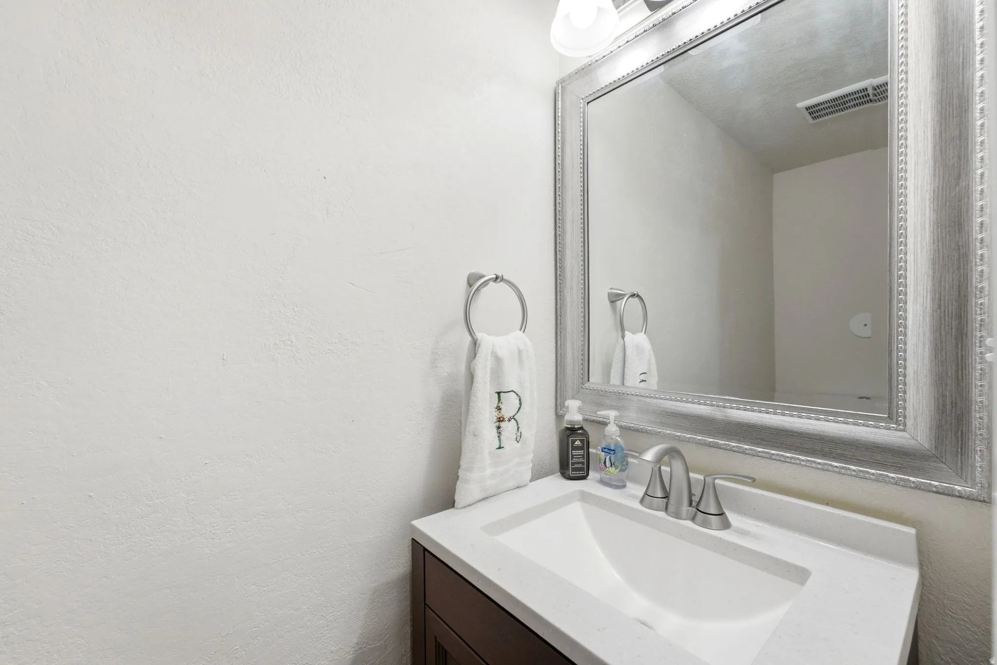 Elegant powder room featuring a white rectangular vessel sink set atop a dark wood-finish vanity, paired with a polished chrome faucet and widespread handles