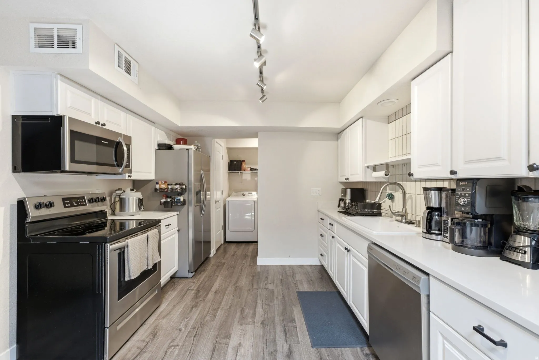 Kitchen featuring white cabinetry, stainless steel appliances, wood-finish flooring, and a tile backsplash