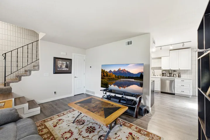 Open-concept living space featuring hardwood flooring, a gas fireplace with built-in entertainment cabinetry, and a well-appointed kitchen with white cabinetry and stainless steel appliances