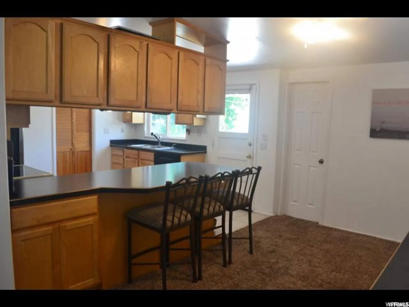 Kitchen featuring wood-finish cabinetry, black countertops, and a pass-through counter