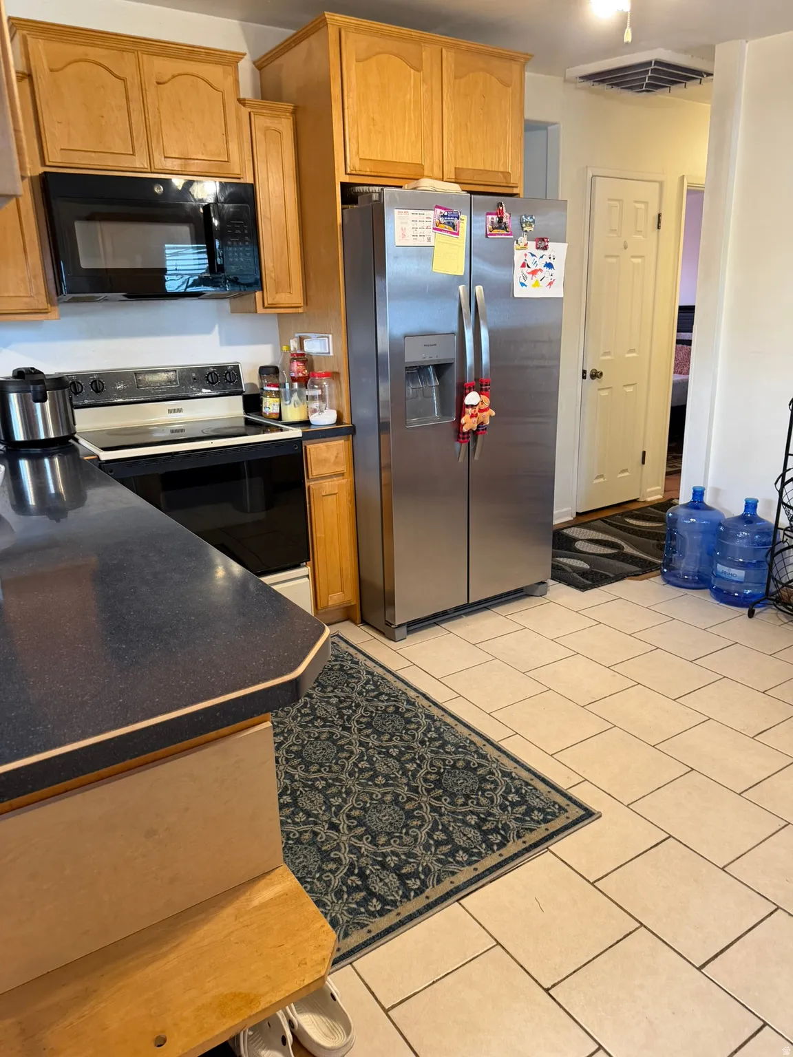 Kitchen featuring light wood cabinetry, a built-in microwave, an electric range, stainless steel French-door refrigerator, and tiled flooring