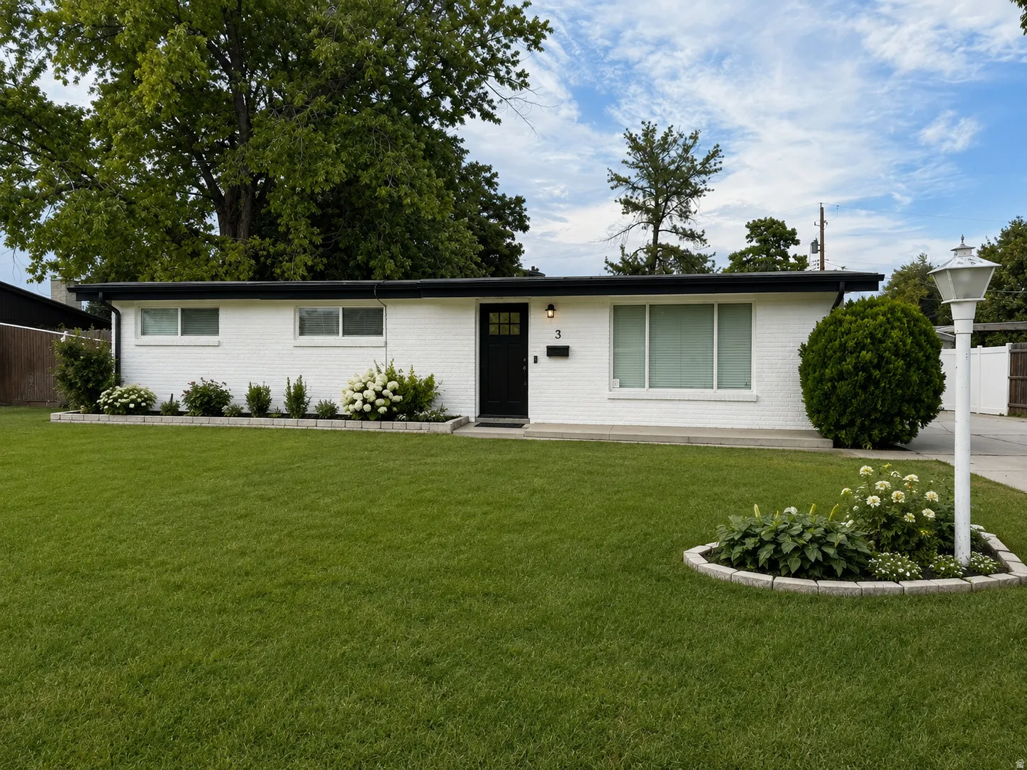 White brick exterior with a black front door, a flat roof, and a prominent front lawn