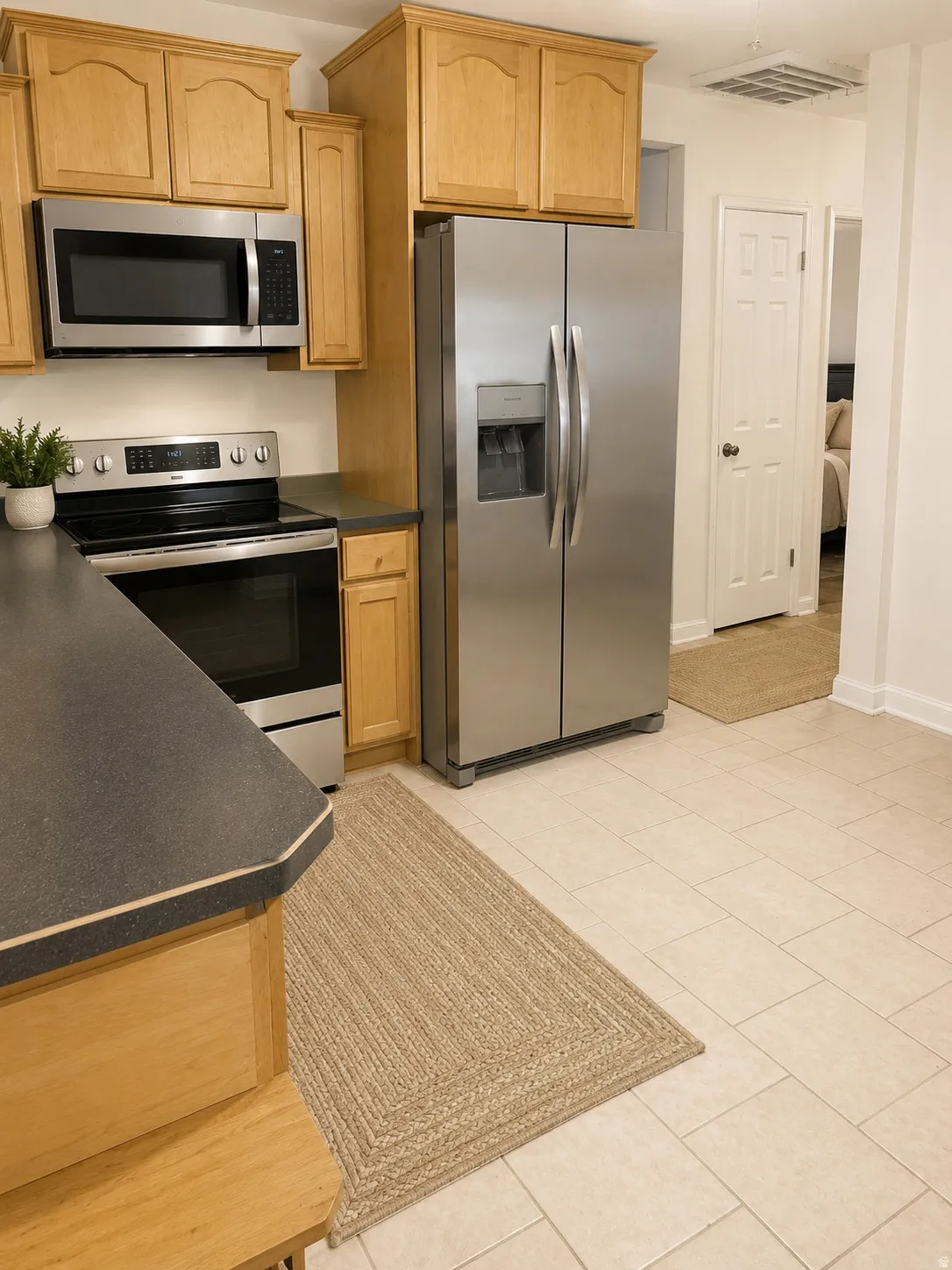 Kitchen featuring light wood cabinetry, stainless steel appliances, dark countertops, and light tile flooring