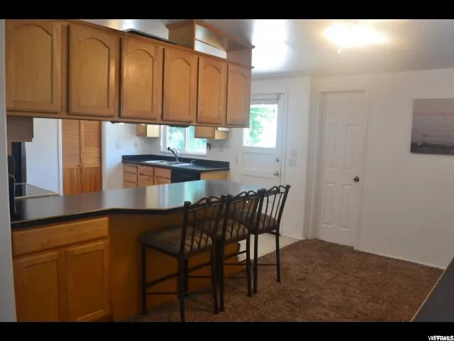 Kitchen featuring wood-finish cabinetry, black countertops, and a pass-through counter