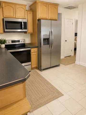Kitchen featuring light wood cabinetry, stainless steel appliances, dark countertops, and light tile flooring
