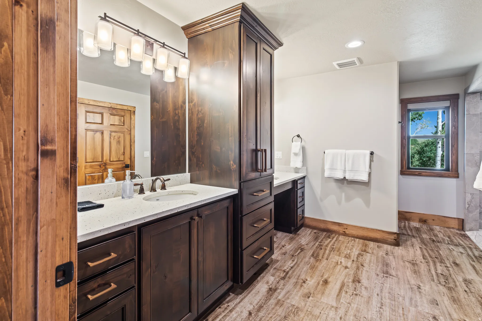 Dual vanity with light-colored countertops, wood-finish flooring, recessed lighting, and a window with wood trim