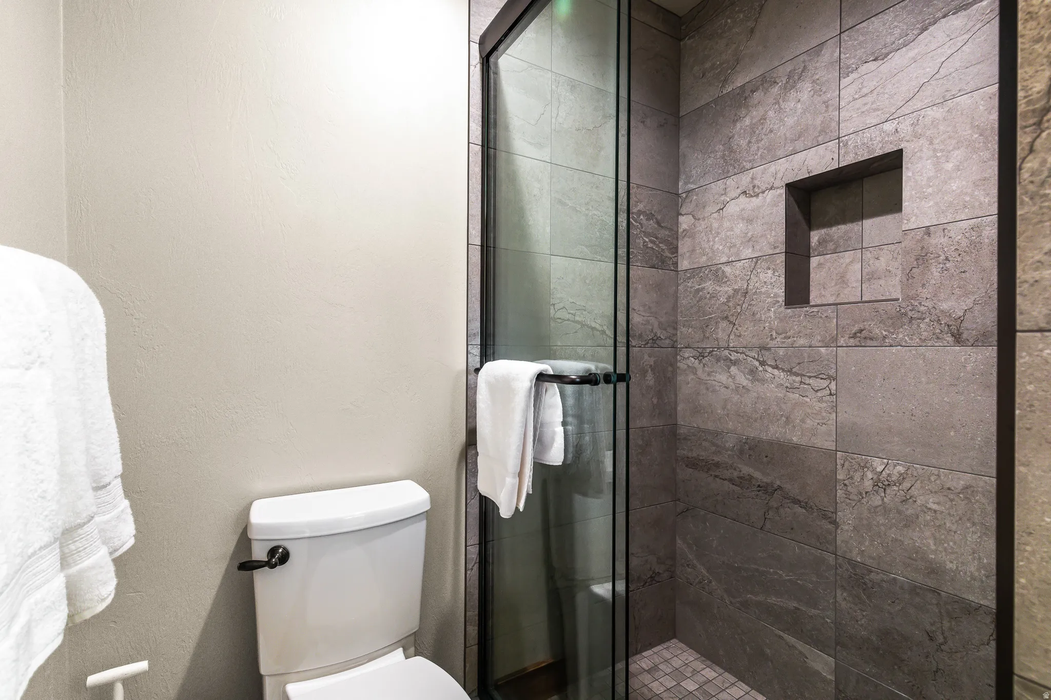 Full glass shower enclosure featuring slate-look tile, built-in shower niche, and mosaic tile shower pan
