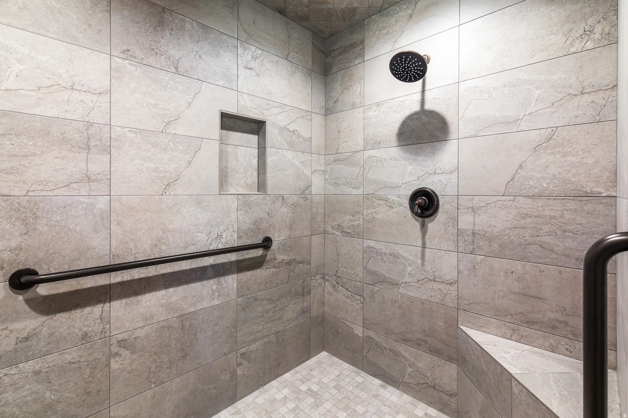 Tiled shower with a built-in bench, recessed niche, black grab bars, and a rain shower head