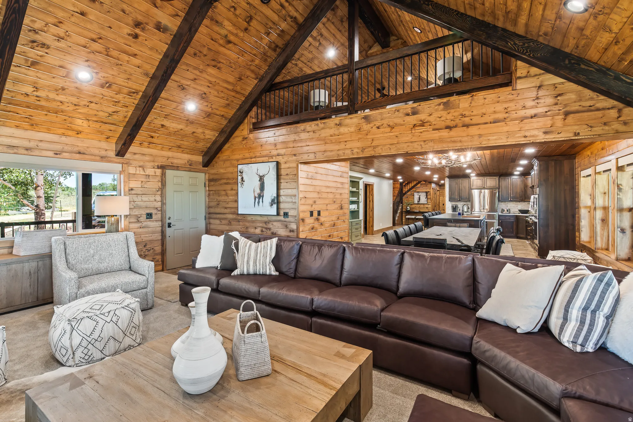 Vaulted wood-paneled ceilings with exposed beams, wood-paneled walls, lofted area with wood railing, recessed lighting, and an open-concept kitchen with wood cabinetry