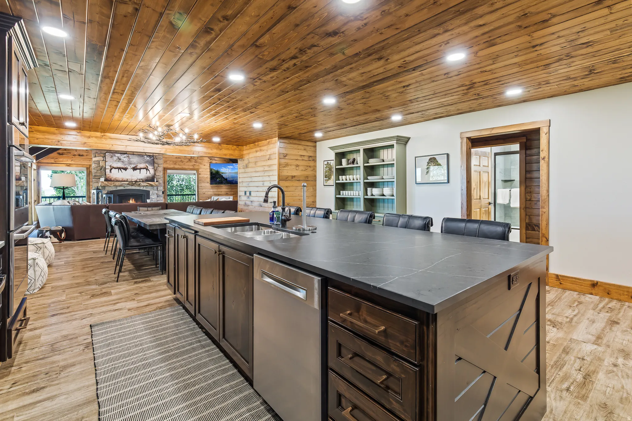 Open-concept living space with wood plank ceiling, stone fireplace, and wood-finish flooring
