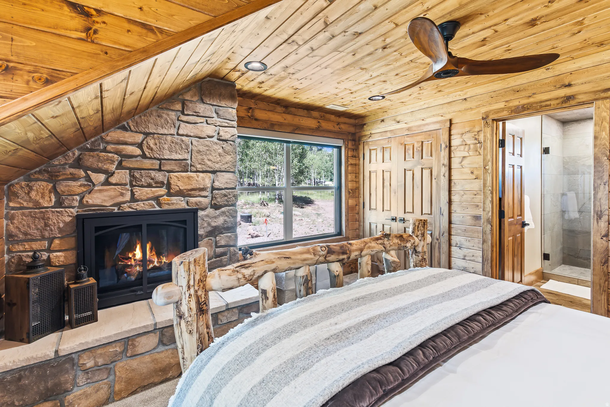 Stone fireplace with a hearth, natural wood paneling, wood-finish ceiling fan, recessed lighting, and a glass-enclosed shower