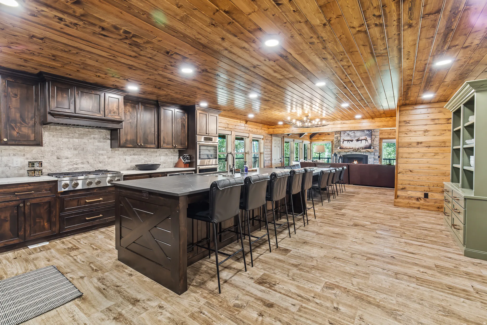Spacious kitchen and dining area featuring a wood plank ceiling, wood-finish flooring, custom dark wood cabinetry, a large kitchen island with counter seating, and a stone backsplash