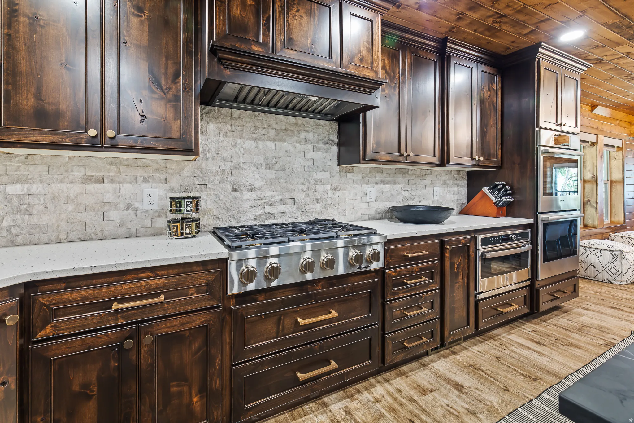Dark wood cabinetry, stainless steel oven, cooktop, and microwave, light-toned stone backsplash, and light-toned countertops