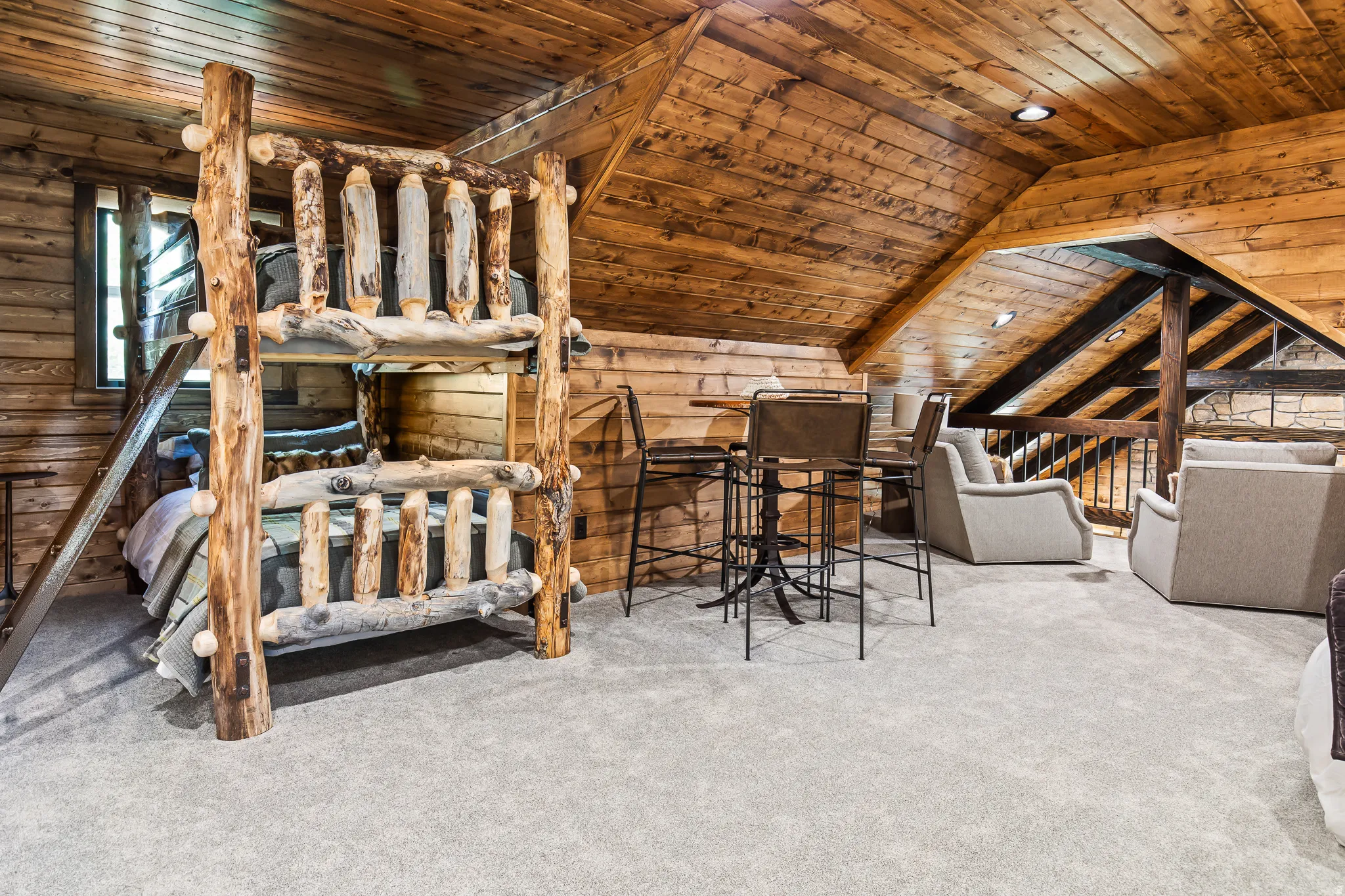 Sloped wood-paneled ceiling, wood-plank walls, light-toned carpet flooring, recessed lighting, and a wood-railing overlook