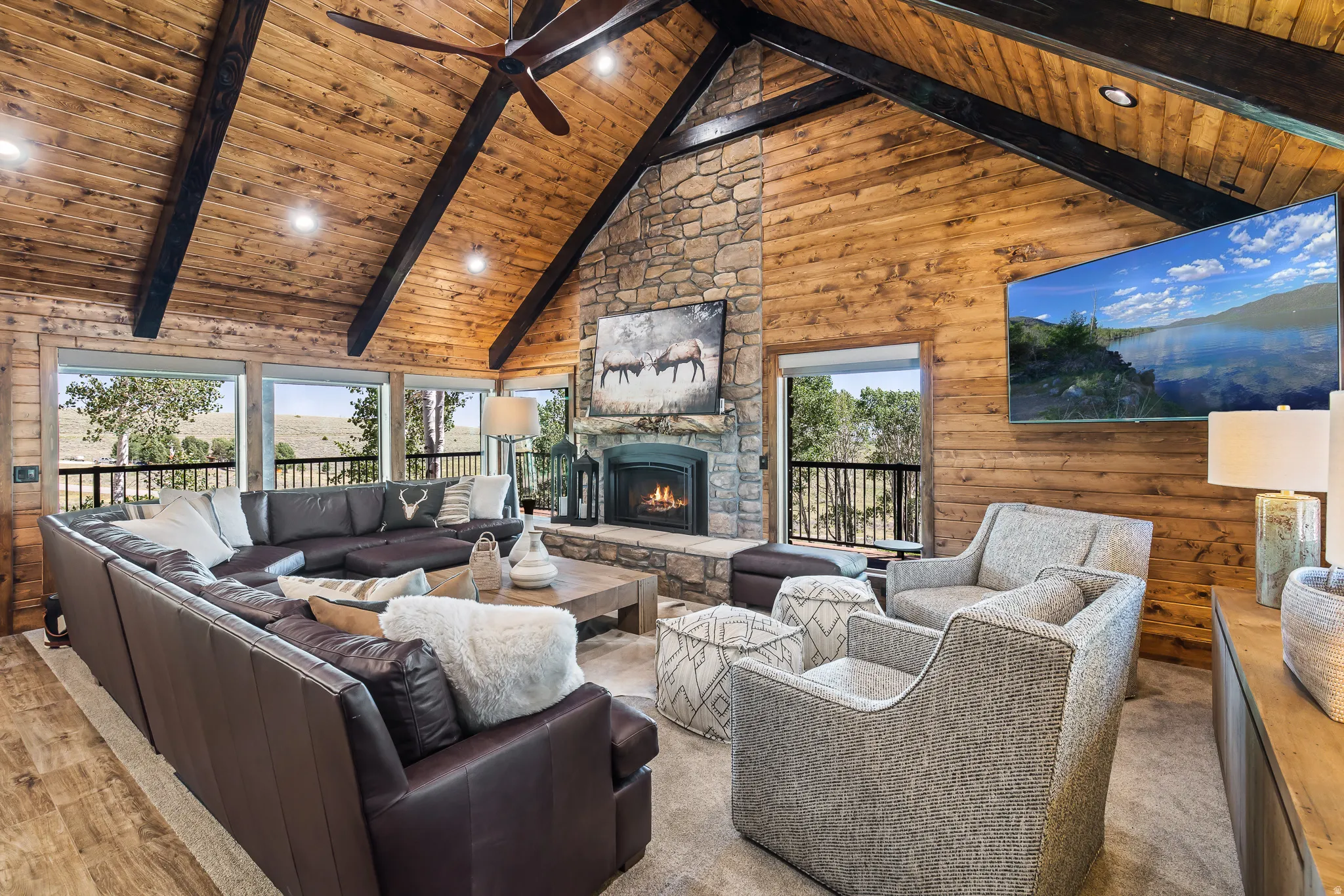 Vaulted wood-paneled ceiling with exposed beams, stone fireplace, wood-finish flooring, and expansive windows