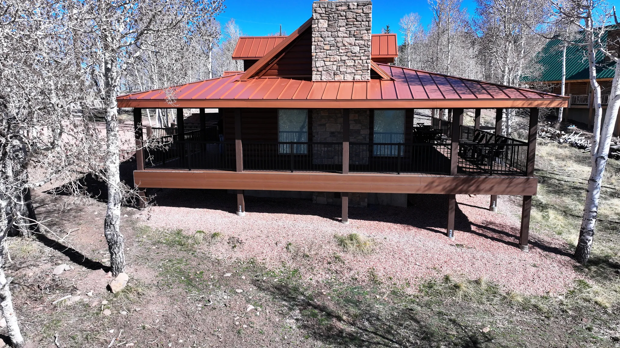 Stone chimney with a brown metal roof, wood siding, and an elevated covered deck featuring black railings