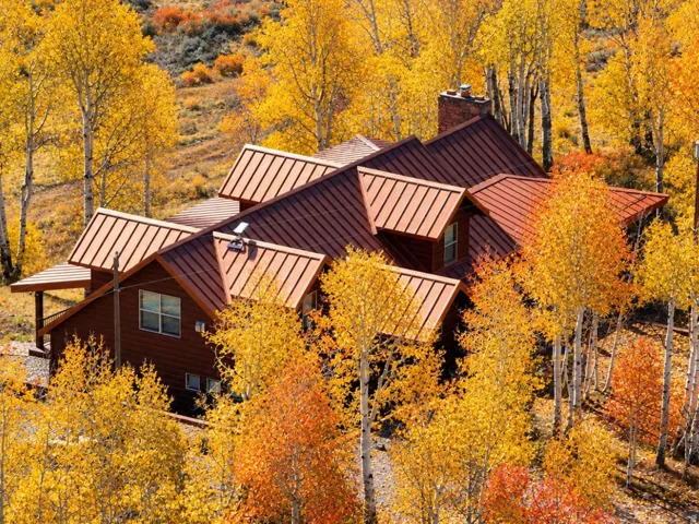 Multi-level residence featuring a brown standing seam metal roof, wood siding, and a prominent brick chimney