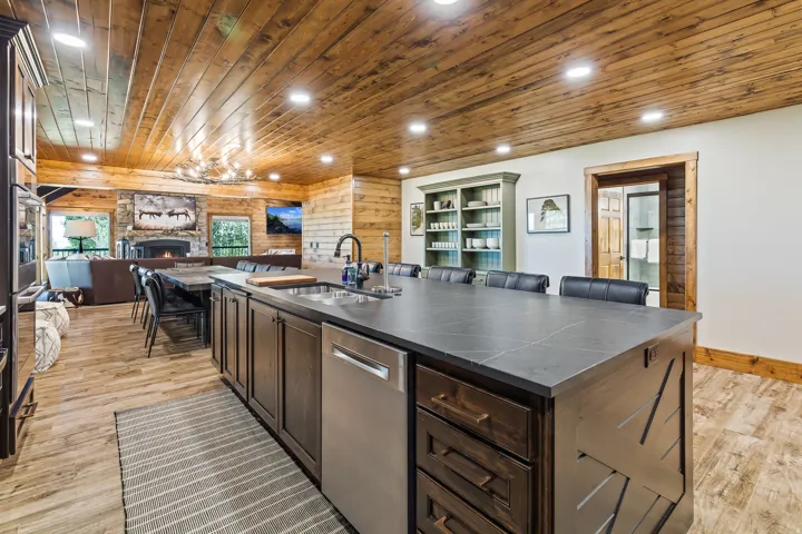 Open-concept living space with wood plank ceiling, stone fireplace, and wood-finish flooring