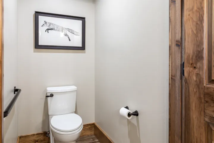 White toilet with dark hardware, wood-finish flooring, and a natural wood door