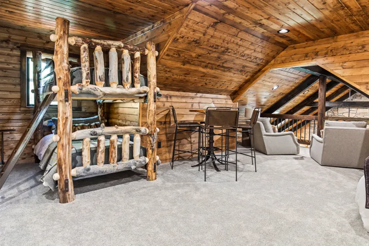 Sloped wood-paneled ceiling, wood-plank walls, light-toned carpet flooring, recessed lighting, and a wood-railing overlook